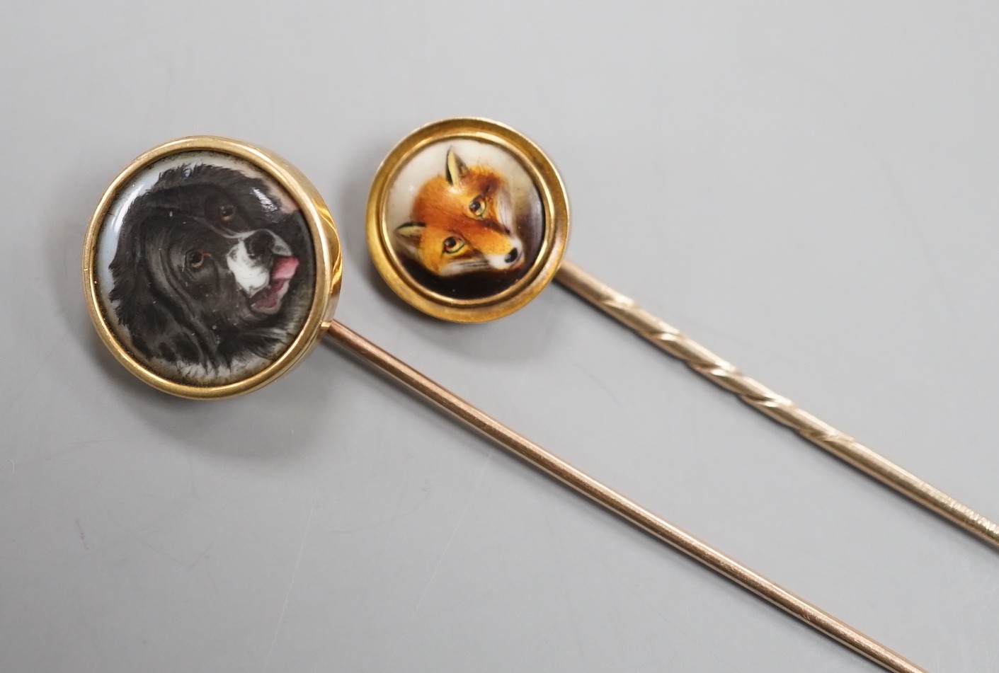 Two early 20th century yellow metal and enamel stick pins, both decorated with the head of a dog, largest, 70mm, gross weight 7.6 grams.
